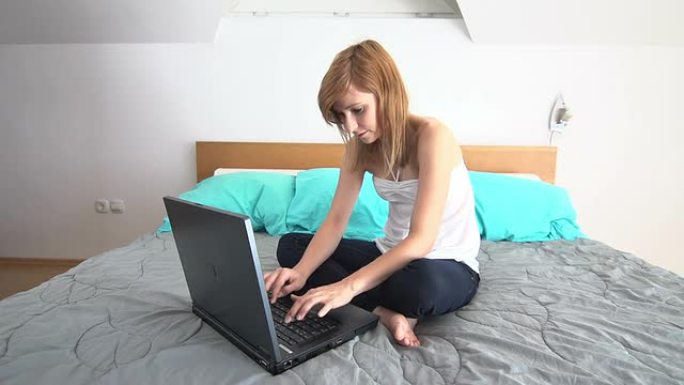 年轻女子坐在床上，用笔记本电脑聊天