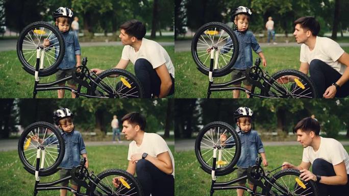 夏天，当他的父亲在公园的草坪上与他交谈时，小男孩正在旋转自行车车轮和踏板。家庭、休闲和积极的生活方式