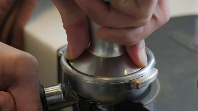 咖啡研磨机的咖啡粉。浓缩咖啡捣固。特写咖啡师通过篡改咖啡将研磨咖啡压入portafilter