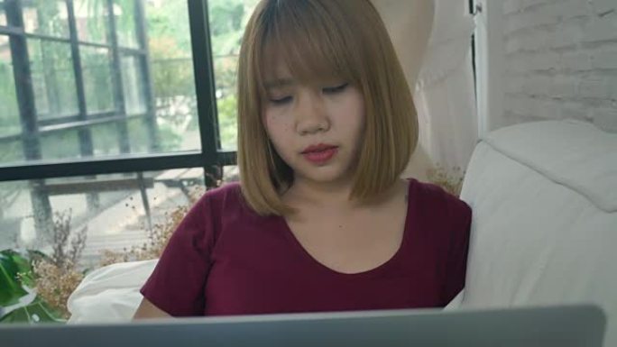 年轻的亚洲女性为她的企业做研究工作。微笑的女人坐在沙发上放松，同时浏览在线购物网站。快乐的女孩在家空