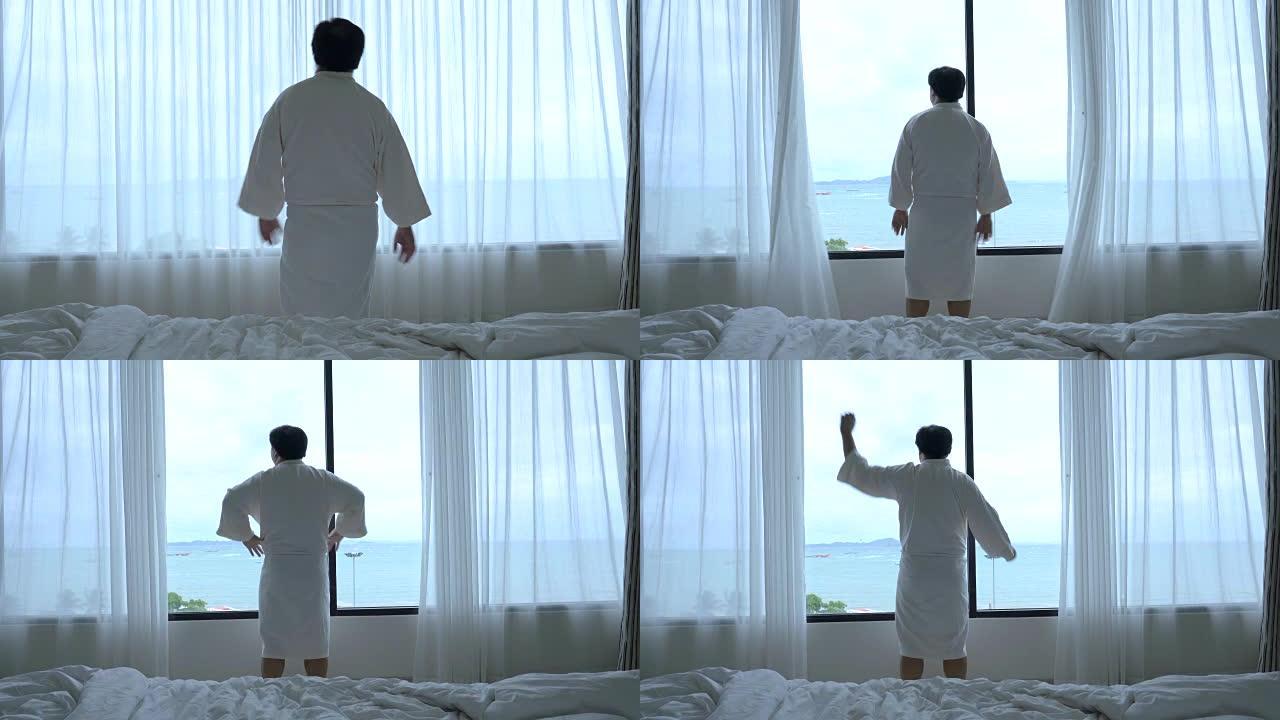4k镜头亚洲男子走路打开窗户窗帘，早上在豪华酒店卧室醒来时伸展自己的场景，生活方式和休闲概念