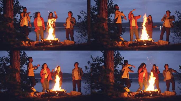兴奋的年轻男女潮人在明亮的篝火旁跳舞，在森林里玩得开心。人、自然和友谊的概念。