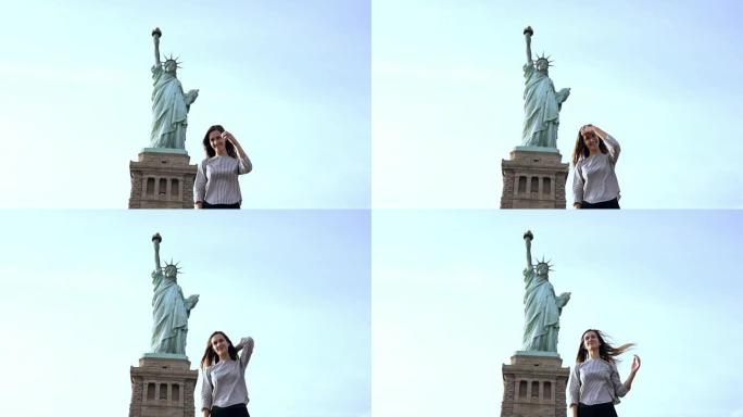 快乐微笑的欧洲女人站在阳光明媚的纽约慢动作中看着相机，对着自由女神像摆姿势