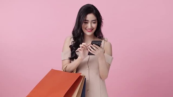 女人在夏天购物。她正在使用智能手机，喜欢购物。孤立在粉红色背景上。