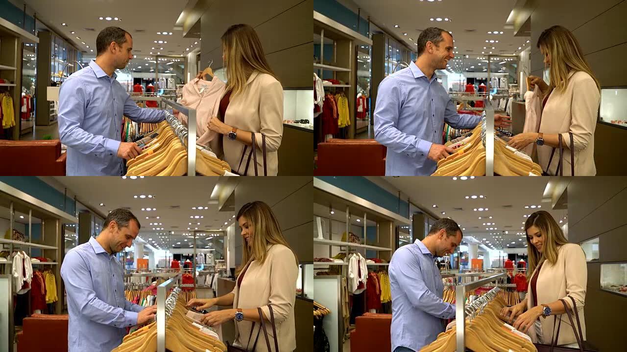 甜蜜的男人在谈话时帮助她的伴侣在服装店找到一件衬衫