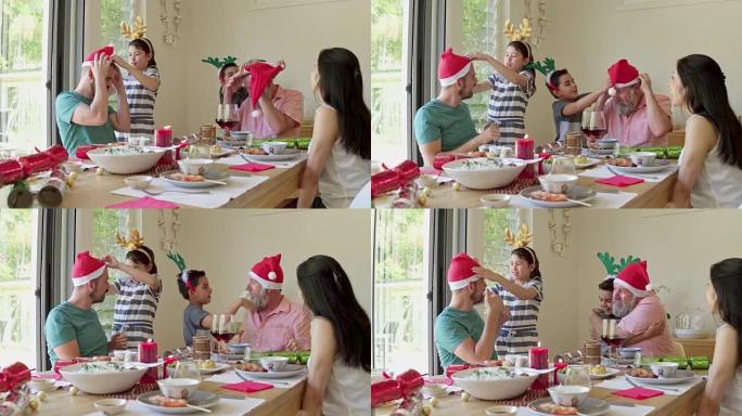 手持视频，孩子们在圣诞节午餐时给父亲和祖父戴上圣诞老人的帽子