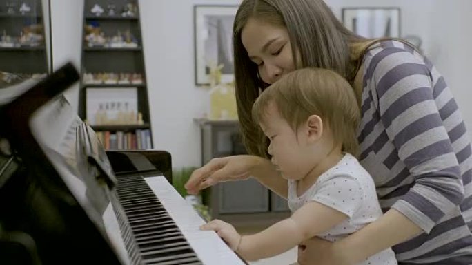 年轻的亚洲母亲和她的男婴弹钢琴