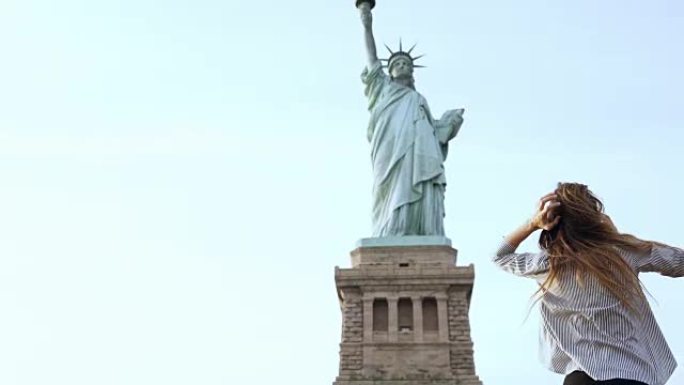 阳光明媚的日子，快乐迷人的微笑着的欧洲旅游女子在纽约自由女神像的电话里交谈