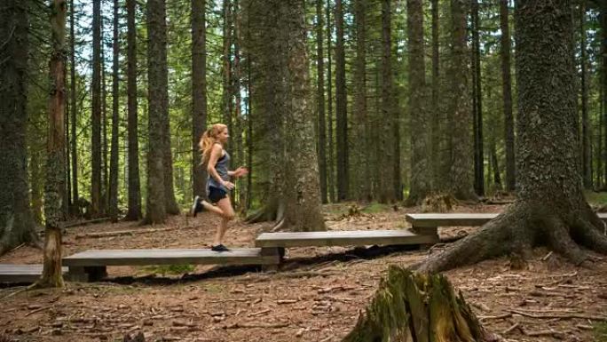 身体意识强的女人在做有氧运动，在树林中的木制道路上奔跑