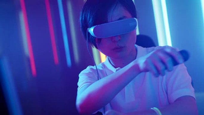 戴着虚拟现实耳机的东亚职业玩家玩带有操纵杆/控制器的在线视频游戏。房间里很酷的复古霓虹灯颜色。