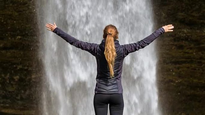 年轻女子在瀑布前的胜利中伸出双臂