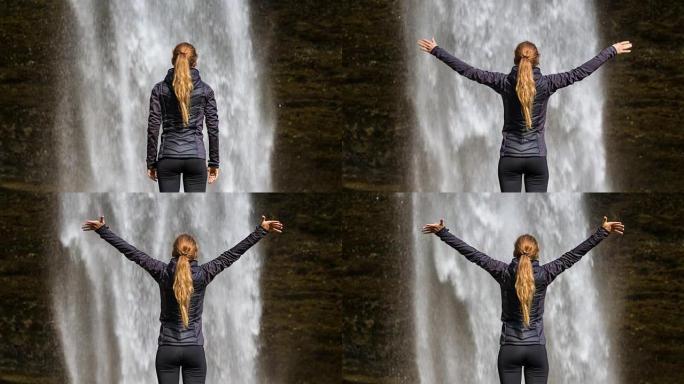年轻女子在瀑布前的胜利中伸出双臂
