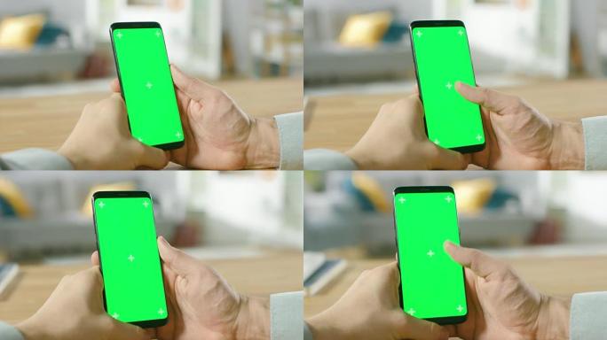 一个男人的特写镜头使用绿色模拟屏幕智能手机，并进行触摸屏手势。触摸手机色度键屏幕。背景中舒适的家常氛