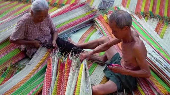 4k镜头场景两位越南老工匠在越南东塔丁延的老传统村庄制作和修剪传统越南垫子的俯视图，传统艺术家概念