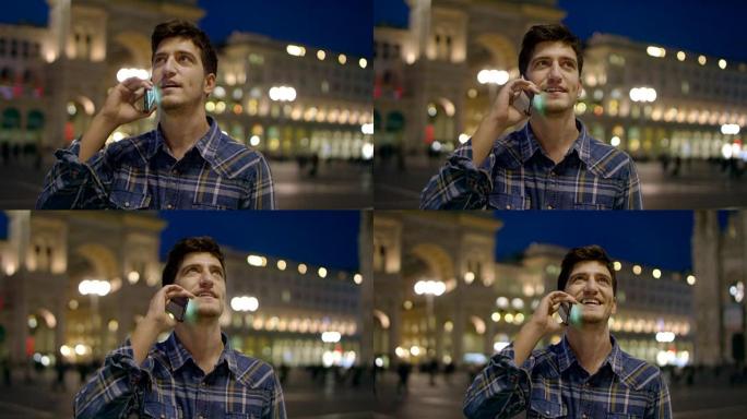 男人看着城市的夜晚。意大利米兰英俊的年轻商人用电话微笑着穿着蓝色衬衫。城市男性。在城市应用程序中使用