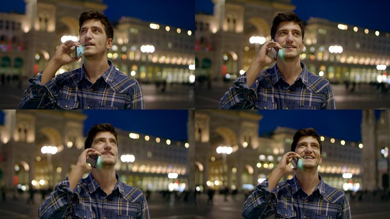 男人看着城市的夜晚。意大利米兰英俊的年轻商人用电话微笑着穿着蓝色衬衫。城市男性。在城市应用程序中使用