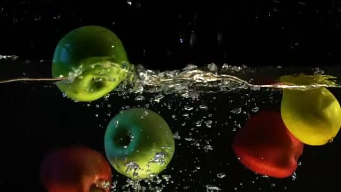 柠檬和苹果落入水中气泡的慢动作视频。孤立的黑色背景上的水果。
