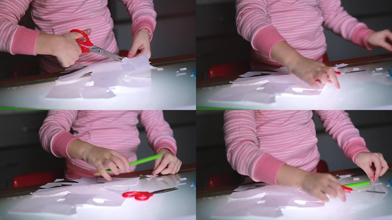 穿着粉红色毛衣的学龄前女孩手的特写镜头用剪刀剪纸和铅笔画画