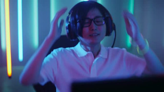 专业的东亚玩家在他的个人电脑上玩在线视频游戏。他输掉了比赛，感到沮丧。复古拱廊风格的霓虹灯点亮的房间