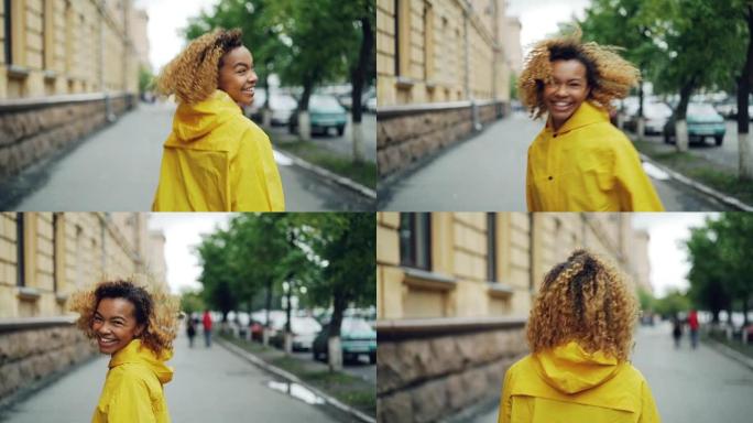 漂亮的年轻女子非洲裔美国学生在街上行走，转身带着快乐的微笑看着相机的慢动作肖像。情感、城市和人的概念