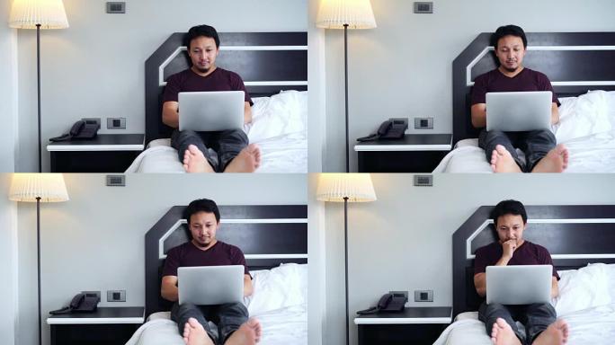 4k镜头亚洲男子休闲西装坐在沙发上思考与科技笔记本电脑一起工作的场景早上在卧室，生活方式和休闲概念