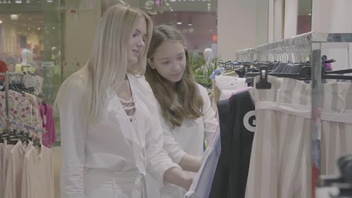 两个女孩在服装店寻找并选择一件衣服