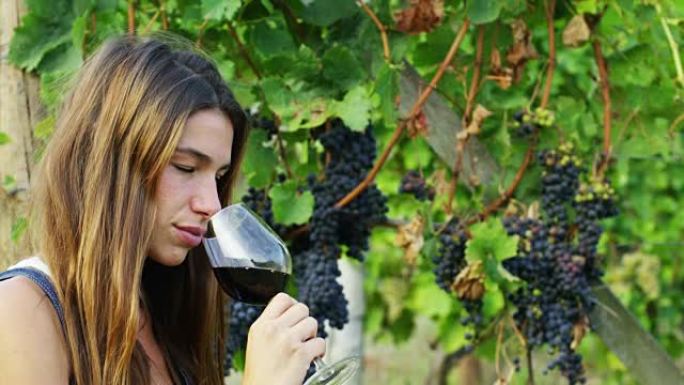 这位年轻女子闻到倒入红葡萄葡萄园背景玻璃杯中的红酒的香气。