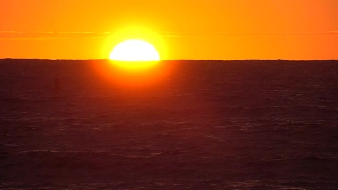 在夏日，慢动作明亮的橙色太阳落在无尽的蓝色海洋后面