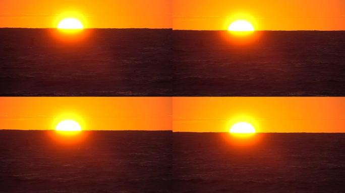 在夏日，慢动作明亮的橙色太阳落在无尽的蓝色海洋后面