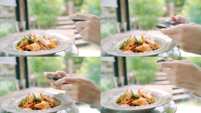 女性博客作者用手机在餐厅拍摄午餐。一名年轻女子在智能手机上拍摄意大利面条食物的照片，用移动相机拍摄饭