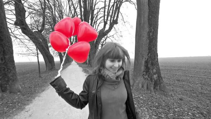 女孩带着红色心形气球在公园里奔跑