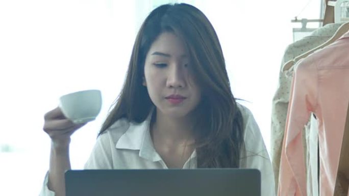 美丽的年轻微笑的女人在笔记本电脑上工作，享受着坐在客厅里喝温暖的咖啡。在家享受时光。在家庭办公室工作