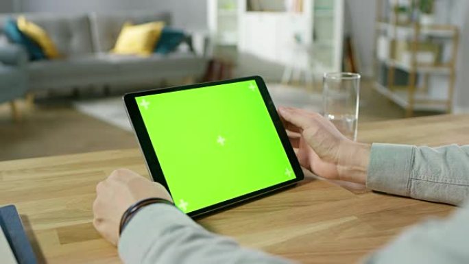 坐在办公桌前的人在绿色模拟屏幕数字平板电脑上握着手势并使用手势。男人买东西或浏览互联网。背景舒适的客