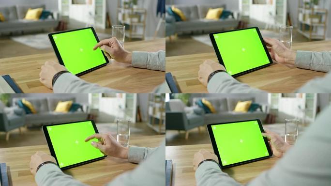 坐在办公桌前的人在绿色模拟屏幕数字平板电脑上握着手势并使用手势。男人买东西或浏览互联网。背景舒适的客