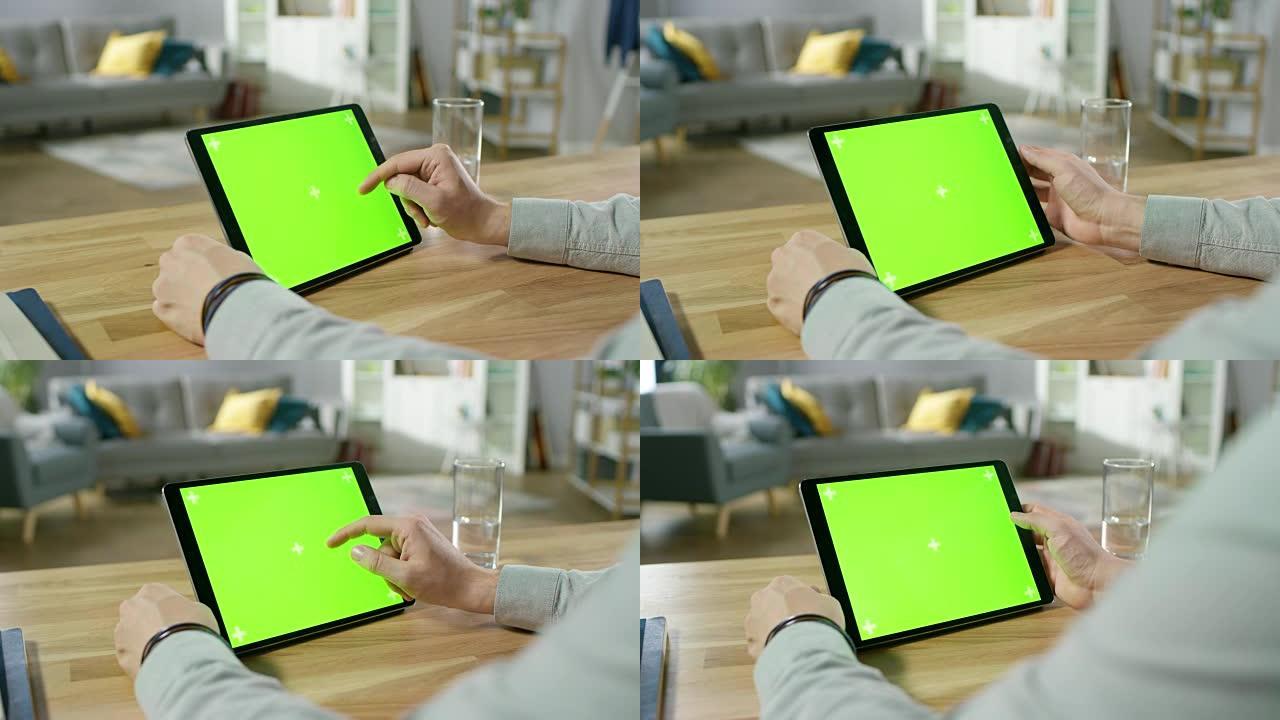 坐在办公桌前的人在绿色模拟屏幕数字平板电脑上握着手势并使用手势。男人买东西或浏览互联网。背景舒适的客