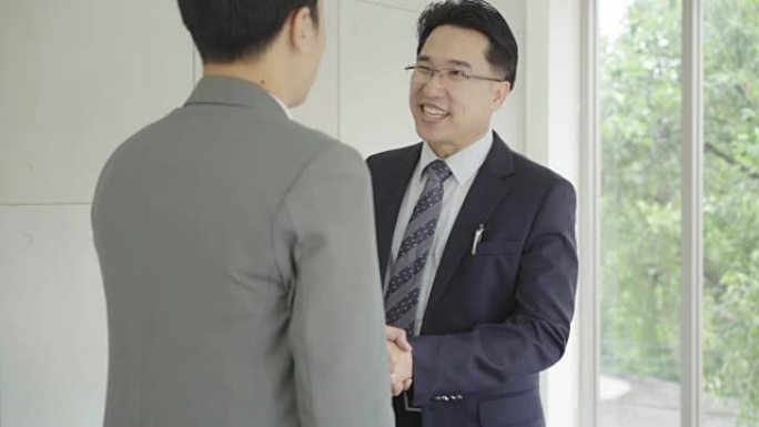 慢动作-求职会议后握手达成协议。两位亚洲自信的商人在办公室开会时握手，成功，交易，问候和合作伙伴概念