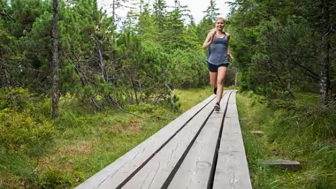 肌肉发达的女运动员在森林中的木制道路上奔跑