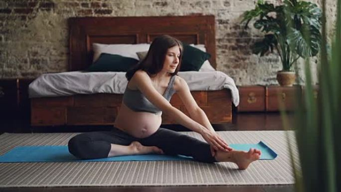 开朗的怀孕女孩正在练习瑜伽，以坐姿向前弯曲一条腿，伸展身体和腿部。积极的生活方式、健康和怀孕理念。