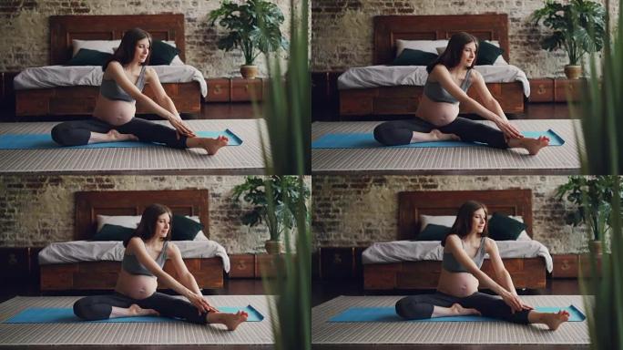 开朗的怀孕女孩正在练习瑜伽，以坐姿向前弯曲一条腿，伸展身体和腿部。积极的生活方式、健康和怀孕理念。