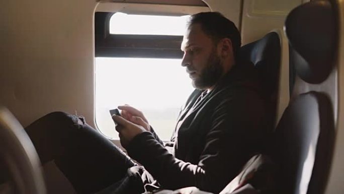自信成功的高加索商人在火车靠窗的座位上旅行时使用智能手机移动办公应用程序