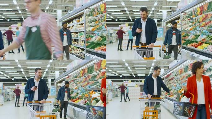 在超市: 英俊的男人带着智能手机，推购物车，穿过商店的新鲜农产品区，选择一些产品。其他购买产品的客户