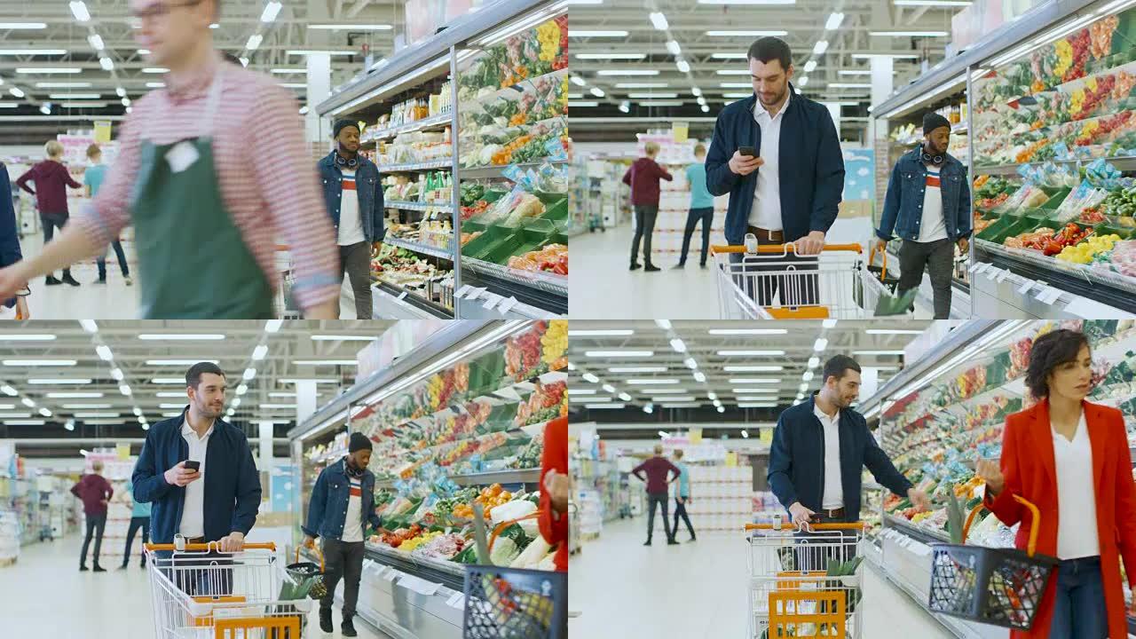 在超市: 英俊的男人带着智能手机，推购物车，穿过商店的新鲜农产品区，选择一些产品。其他购买产品的客户