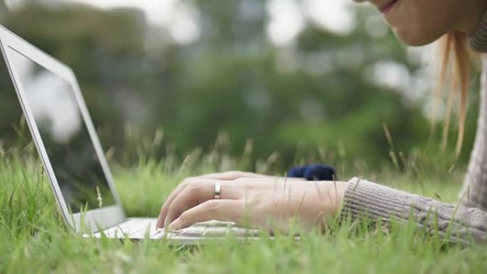 年轻女子在公园的笔记本电脑上打字，特写