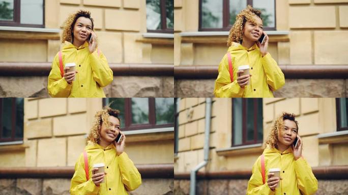 粗心的非洲裔美国女孩正在用手机聊天，拿着外卖咖啡站在现代城市的户外。通信和技术概念。