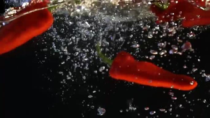 辣椒被扔进一个盛水的容器里。慢动作视频。