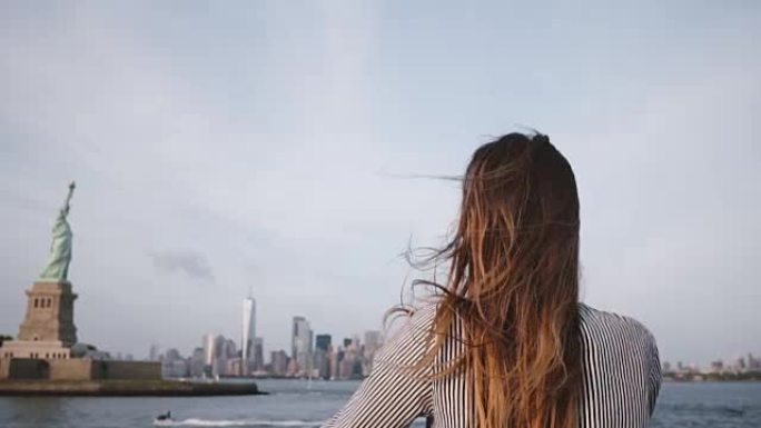 快乐的旅行者女人，头发在风中吹，在自由女神像的船上享受纽约天际线慢动作