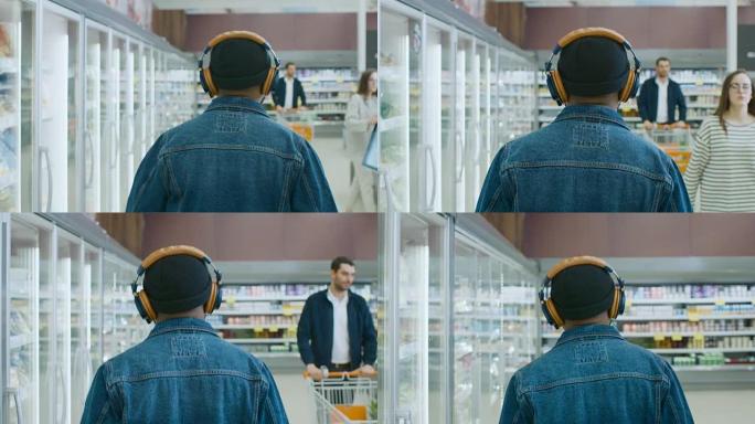 在超市:时尚的非洲裔美国人戴着耳机走过商店的冷冻商品区。后面的视图拍摄。缓慢的运动。