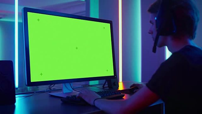 职业玩家在他的个人电脑上的绿色模拟屏幕上玩视频游戏。通过耳机上的麦克风与他的团队交谈。复古霓虹灯室。