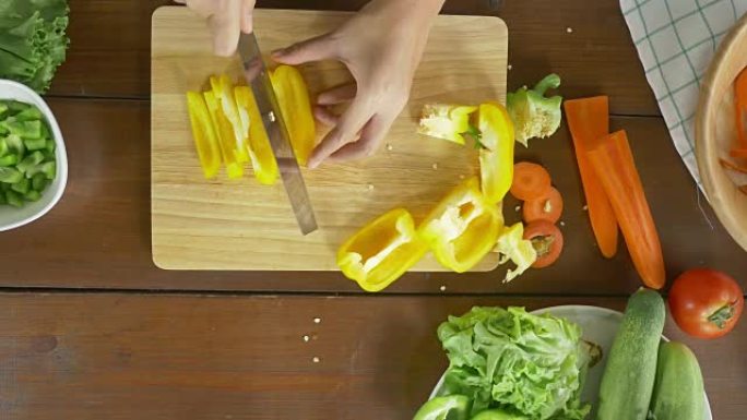 女酋长在厨房的切菜板上制作沙拉健康食品和切碎甜椒的俯视图。
