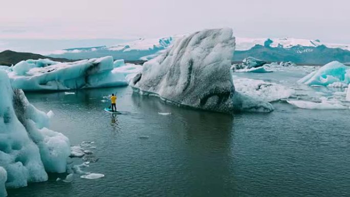 站在巨大冰山上的冰川泻湖中划桨的板子的鸟瞰图